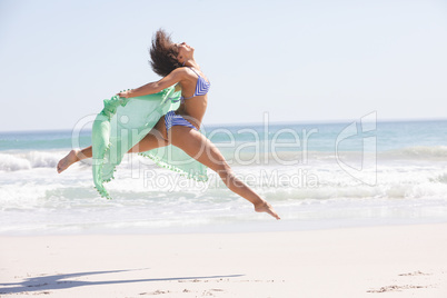 Woman in bikini with scarf jumping on the beach