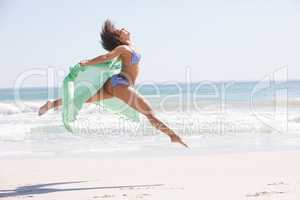 Woman in bikini with scarf jumping on the beach