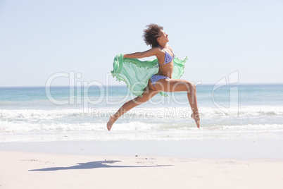 Woman in bikini with scarf jumping on the beach