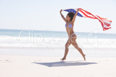 Woman in bikini with american flag running on the beach