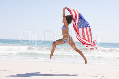 Woman in bikini with american flag jumping on the beach