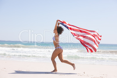 Woman in bikini with american flag running on the beach