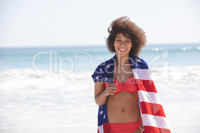 Woman wrapped in american flag looking at camera on the beach