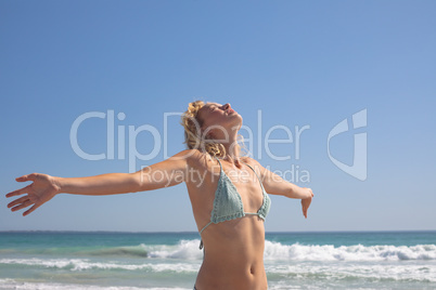 Woman in bikini with arm stretched out standing on the beach