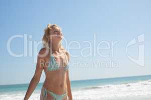 Woman in bikini with eyes closed standing on the beach