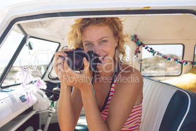 Woman taking photo with digital camera in camper van at beach