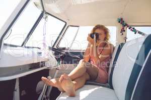 Woman taking photo with digital camera in camper van at beach