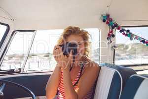 Woman taking photo with digital camera in camper van at beach