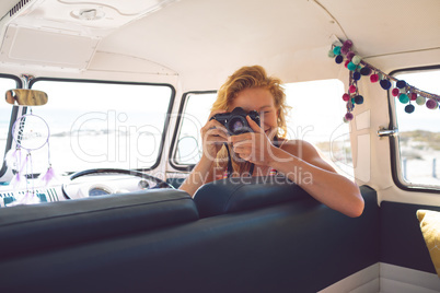 Woman taking photo with digital camera in camper van at beach