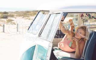 Woman taking selfie with mobile phone while lying on seat in camper van at beach