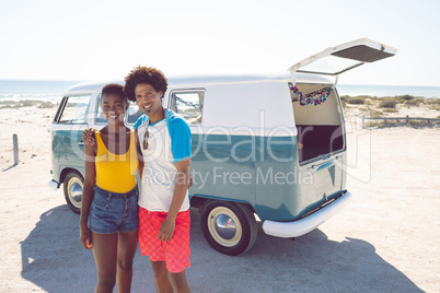 Couple looking at camera while standing near camper van at beach