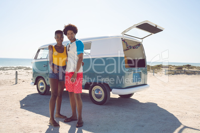 Couple looking at camera while standing near camper van at beach