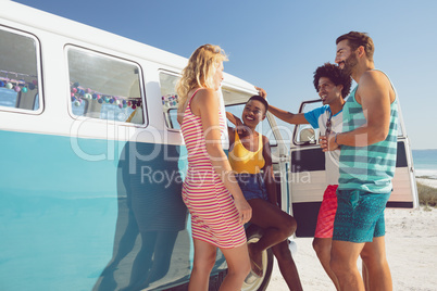 Group of friends talking with each other near camper van at beach in the sunshine
