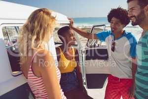 Group of friends talking with each other near camper van at beach in the sunshine