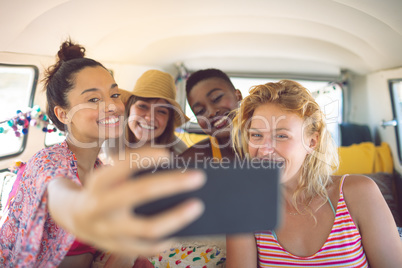 Group of female friends taking selfie with mobile phone in a camper van at beach