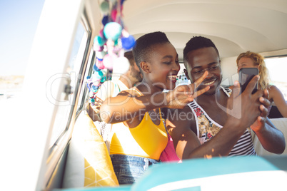 Friends taking selfie on mobile phone in camper van at beach