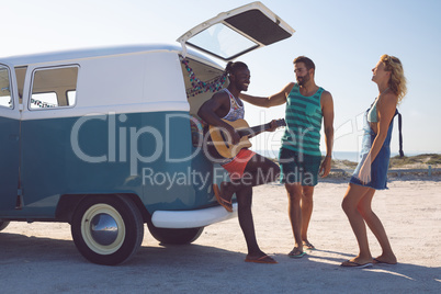 Group of friends having fun together near camper van at beach