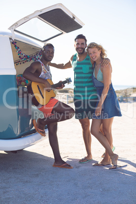 Group of friends having fun together near camper van at beach