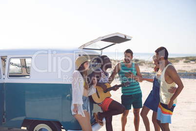 Group of friends having fun together near camper van at beach