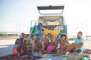 Group of friends looking at camera while sitting near camper van at beach
