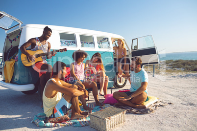 Group of friends having fun near camper van at beach