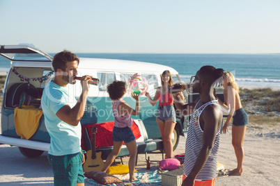 Group of friends having fun near camper van at beach