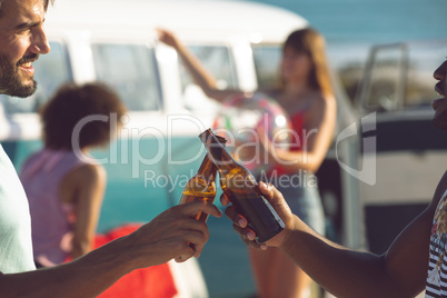 Male friends toasting beer bottle near camper van at beach