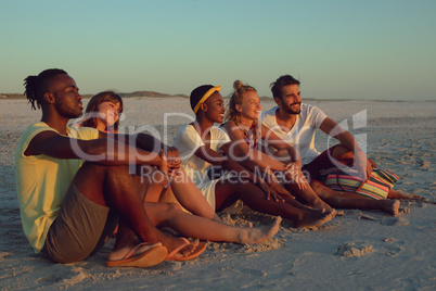 Friends sitting together on the beach during sunset