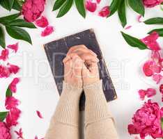 two hands lie on the old book in a gesture of prayer
