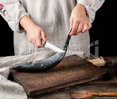 woman in gray linen clothes cleans the fish sea bass
