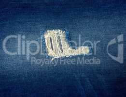 fragment of blue jeans fabric with a hole, full frame