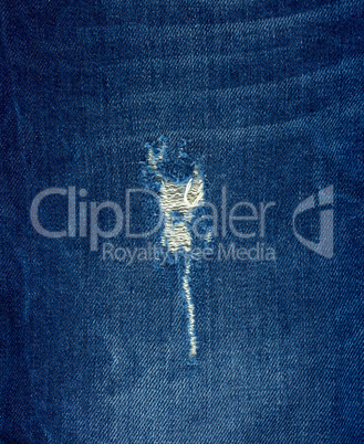 fragment of blue jeans fabric with a hole, full frame