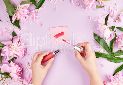 female hands with smooth fair skin keep liquid red lipstick in a