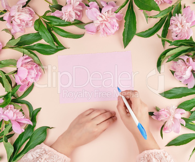 female hand holds hand a white pen over empty pink sheet of pape