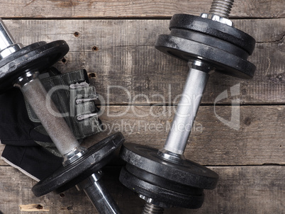 Gloves with dumbbells on wood, top view