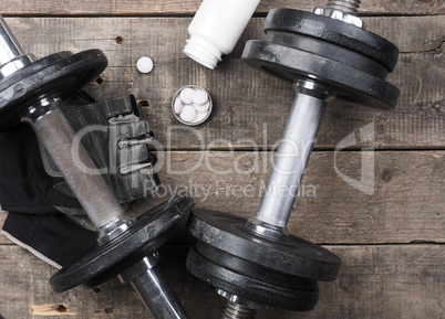 Protein pills with dumbbells on wood, top view