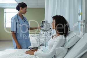 Female doctor adjusting medical monitor while female patient sitting on bed in the ward