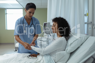 Female doctor attaching iv drip on female patient hand in the ward