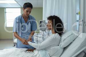 Female doctor attaching iv drip on female patient hand in the ward
