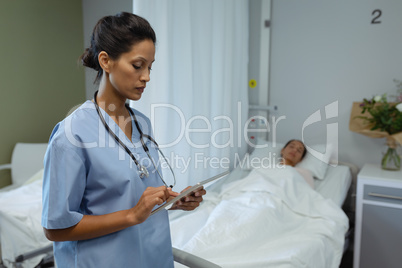 Female doctor using digital tablet while patient sleeping in bed in the ward