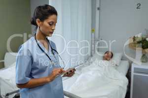 Female doctor using digital tablet while patient sleeping in bed in the ward