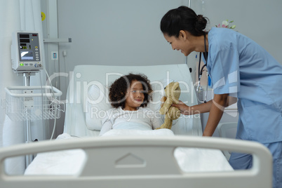 Female doctor giving teddy bear to child patient in the ward