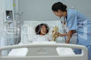 Female doctor giving teddy bear to child patient in the ward