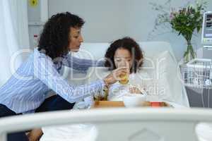 Mother feeding her son orange juice in bed in the ward