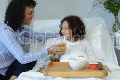 Mother feeding her son orange juice in bed in the ward