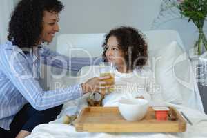 Mother feeding her son orange juice in bed in the ward