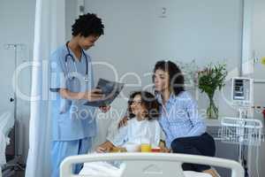 Female doctor discussing over x-ray report with mother and son in the ward