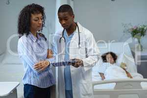 Male doctor discussing over clipboard with woman in the ward
