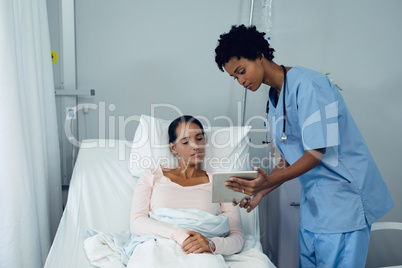 Female doctor showing medical report to female patient on digital tablet in the ward