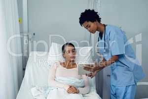 Female doctor showing medical report to female patient on digital tablet in the ward